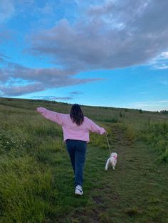 a woman is walking her dog on a leash in the grass with clouds behind her