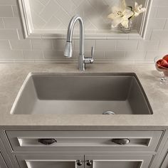 a kitchen sink sitting under a faucet next to a vase with flowers in it