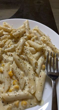 a white plate topped with macaroni and cheese covered in seasoning next to a fork