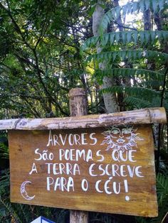 a wooden sign with writing on it in front of some trees and plants at the park