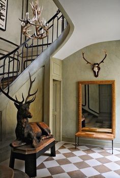 a deer statue sitting on top of a wooden bench next to a stair case and mirror