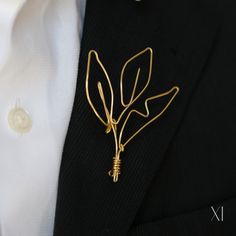 a man wearing a black suit and white shirt with a gold leaf brooch on his lapel