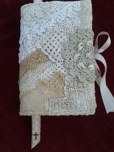 an old book with lace and ribbon on it sitting on a red cloth covered table