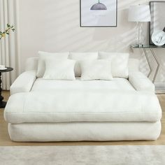 a large white couch sitting on top of a wooden floor next to a table and lamp