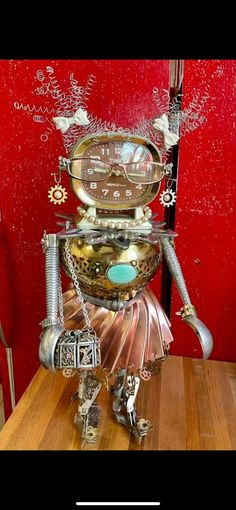 a robot made out of metal parts on top of a wooden table next to a red refrigerator