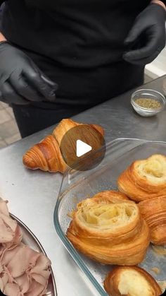 a person in black gloves preparing pastries on top of a metal counter with other food items