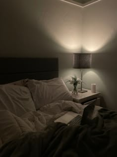 a laptop computer sitting on top of a bed next to a night stand and lamp