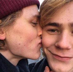 two young men are kissing each other while one is wearing a beanie and the other has his eyes closed