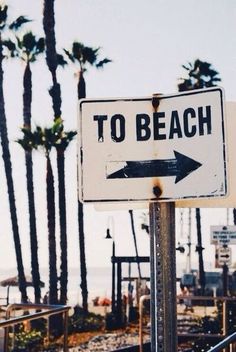 a street sign that says to beach and an arrow pointing in opposite directions with palm trees in the background