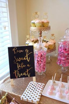 a table topped with lots of candy and cupcakes next to a sign that says love is sweet take a treat