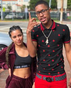 a man and woman standing next to each other in front of a car, making the peace sign