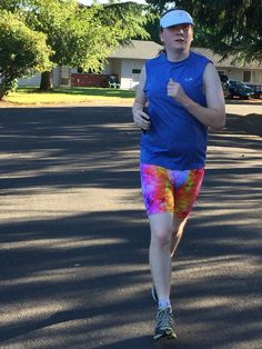 a man running in the street wearing colorful shorts and a blue shirt with tie dye on it