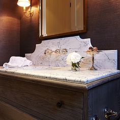 a bathroom with a marble counter top and wooden cabinetry, lighted by two lamps