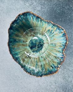 a blue and green bowl sitting on top of a cement floor next to a white wall