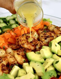 someone is pouring dressing on some shrimp and veggies in a glass bowl with cucumbers