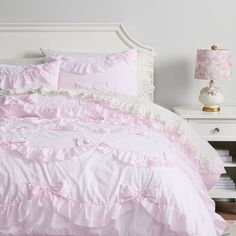 a white bed with pink ruffled sheets and pillows