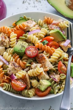 a white bowl filled with pasta salad next to an avocado and tomato slice