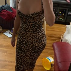 a woman in a leopard print dress taking a selfie with her cell phone and drinking from a yellow cup