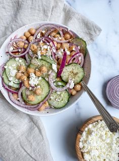 a salad with cucumbers, onions and chickpeas in a white bowl