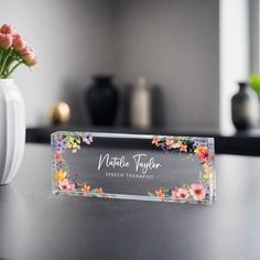 a vase with some flowers in it sitting on a table next to a name plate