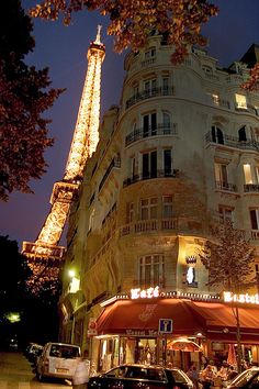 the eiffel tower is lit up at night with cars parked in front of it