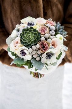 a bridal bouquet with succulents and other flowers is held by a woman in a fur coat