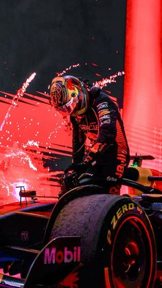 a man standing on top of a racing car in front of red lights and fireworks