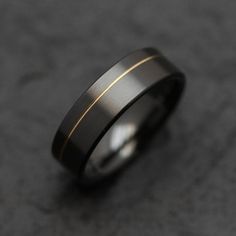 a black and gold wedding ring on a gray surface with two lines in the middle