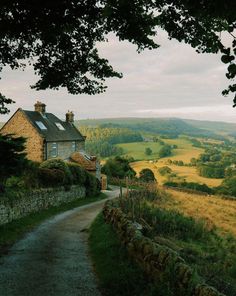 an old stone house on the side of a country road with fields in the background