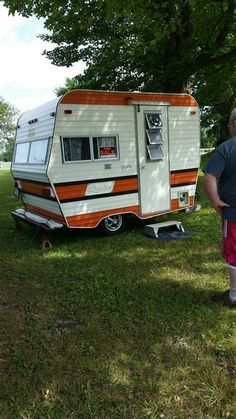 a man standing next to an rv in the grass