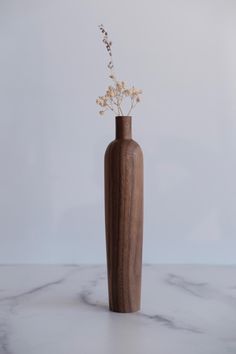 a wooden vase with flowers in it sitting on a marble countertop next to a white wall