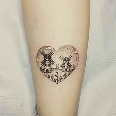 a heart shaped tattoo on the leg of a person with trees and mountains in it