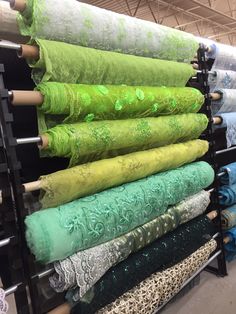 an array of different colored fabrics are on display in a store with metal racks holding them