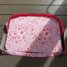 a pink and red flowered tray sitting on top of a wooden table next to a person's shadow