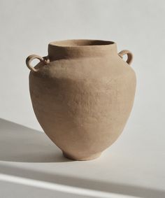 a large clay vase sitting on top of a white table next to a shadow from the wall