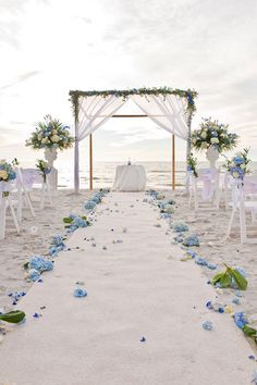 an outdoor wedding setup on the beach with blue flowers and white draping over the aisle