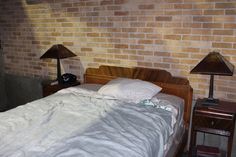 a bed sitting next to a brick wall with two lamps on either side of it