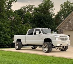 a white pickup truck parked in front of a house with large tires on it's rims