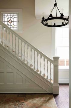 a chandelier hanging from the side of a white stair case next to a window