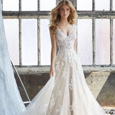 a woman in a wedding dress is standing near a window and posing for the camera