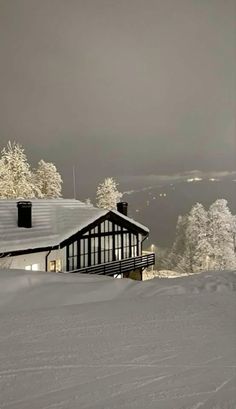 a house on top of a snow covered hill with trees in the background and dark sky