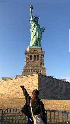 a woman standing in front of the statue of liberty, with her arms raised up