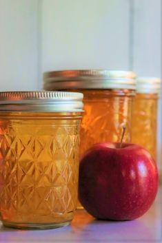 three jars filled with apples sitting on top of a white counter next to an apple