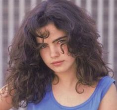 a close up of a person wearing a blue shirt and long curly hair with an intense look on her face