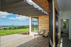 a wooden deck with two chairs and a table next to a glass door that leads out onto a grassy field