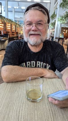 an older man sitting at a table with a glass and cell phone in front of him