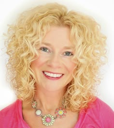 a woman with blonde hair and blue eyes smiles at the camera while wearing a pink shirt