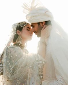 a man and woman dressed in white are kissing each other with veils on their heads