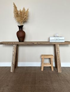 a wooden table with a vase and two stools next to it on the floor