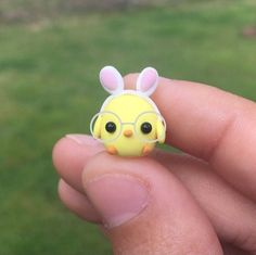 a tiny yellow chick wearing glasses is sitting on someone's finger with grass in the background